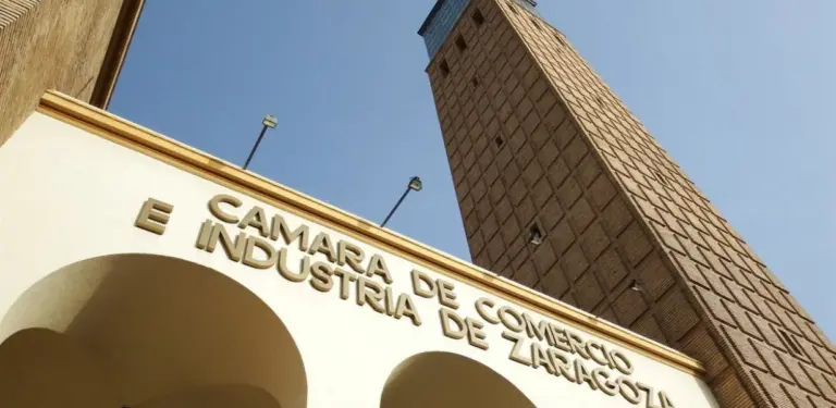 Fachada del edificio de la Cámara de Comercio e Industria de Zaragoza bajo un cielo despejado, representando la colaboración de John Pye Subastas España con la institución aragonesa.